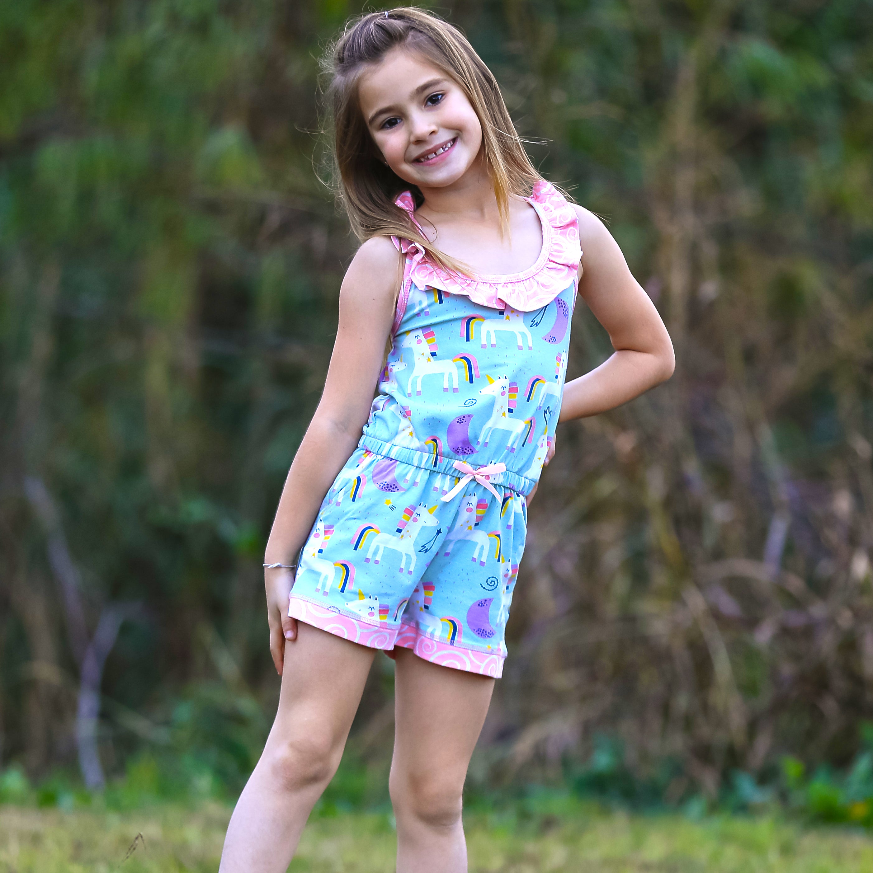 AnnLoren Little & Big Girls Jumpsuit featuring a magical unicorn and rainbow print, with pink swirl ruffle neckline and criss-cross straps.